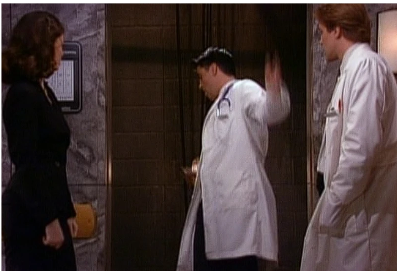 Joey, in a doctor's coat, waiting at an elevator.